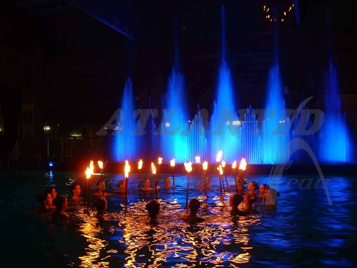 Atlantid - Espectáculo nocturno de chorros de agua azul con gente en el agua al frente con llamas de mano